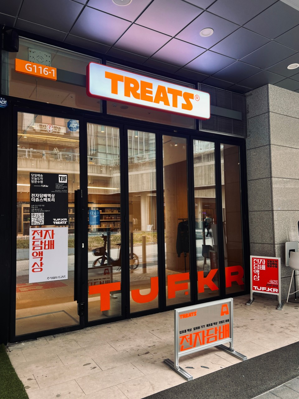 TREATS 오프라인 매장 전면: 주황색 간판과 유리 출입문의 TJF.KR 표기